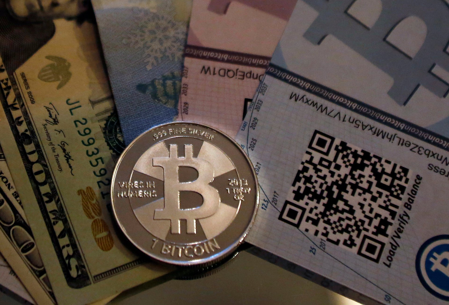 Physical representation of bitcoin alongside US dollars and cryptocurrency QR codes, illustrating currency exchange and financial transactions